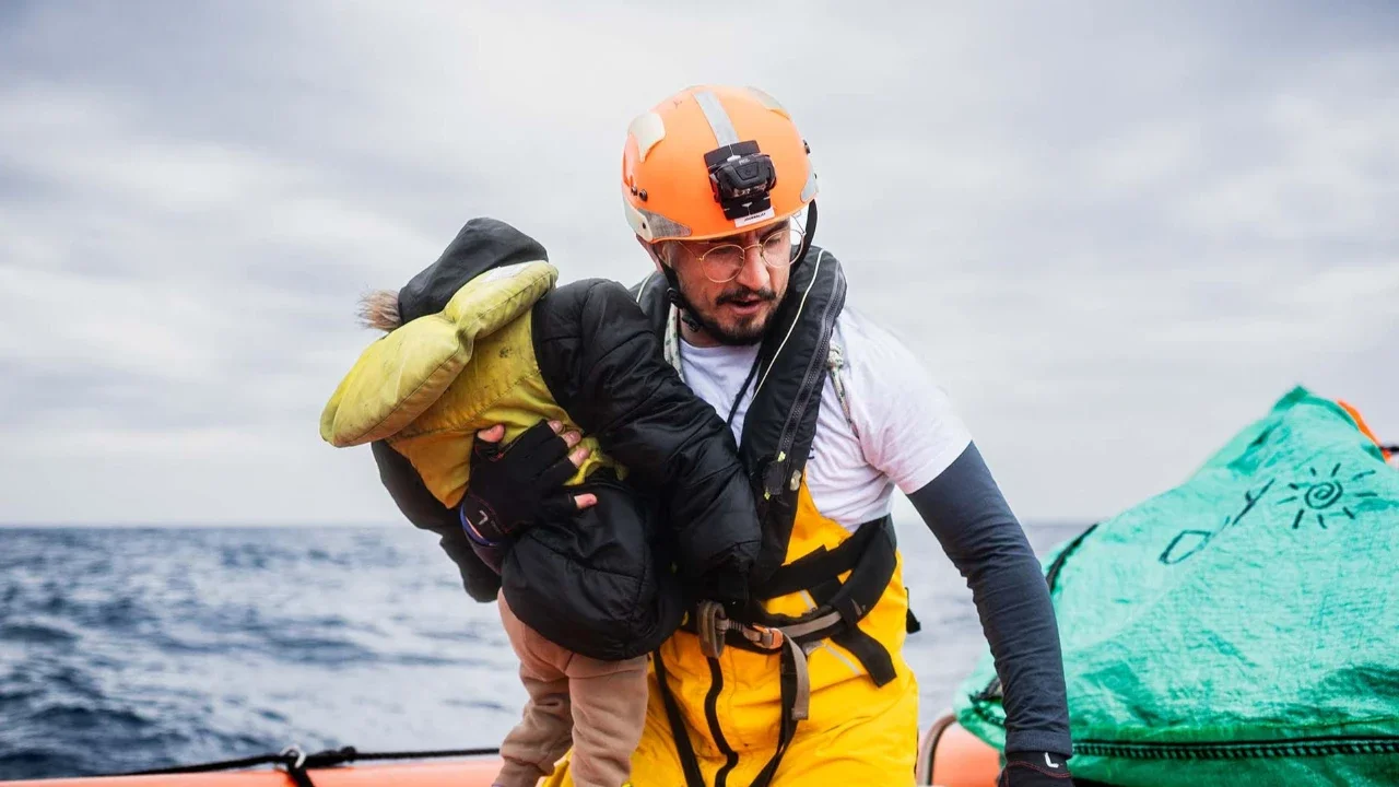 Seorang anggota kru kapal penyelamat “Ocean Viking” menggendong seorang anak kecil di atas perahu karet (RHIB) mereka selama operasi penyelamatan di zona pencarian dan penyelamatan di lepas perairan internasional Libya, Jumat (16/01/2026).