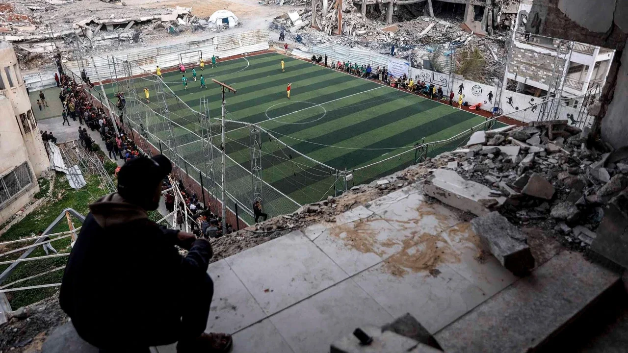 Warga Palestina menyaksikan pertandingan sepak bola lima lawan lima di tengah reruntuhan bangunan yang hancur di Kota Gaz, Senin (09/02/2026) waktu setempat.