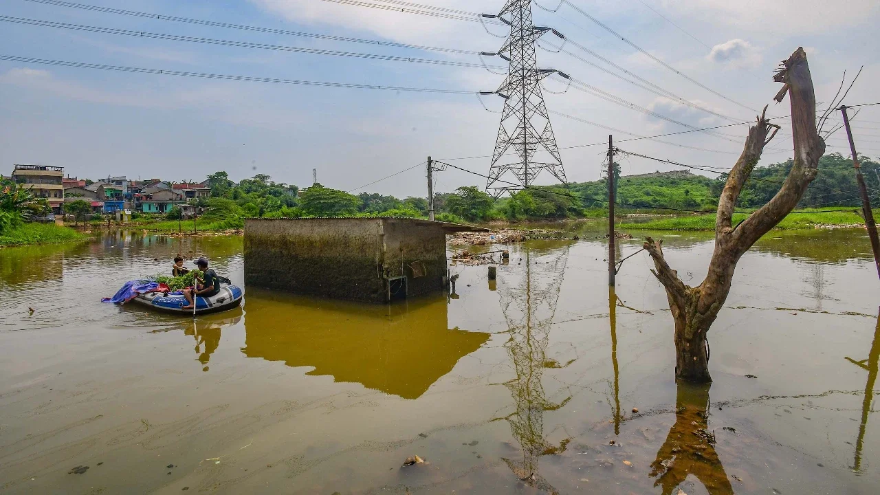 Warga membwa rumput dengan perahu karet melewati rumah warga yang kosong akibat tergenang Kali Pesanggrahan yang alirannya menyempit karena longsoran TPA Cipayung di kawasan Cipayung, Depok, Kamis (14/05/2026).