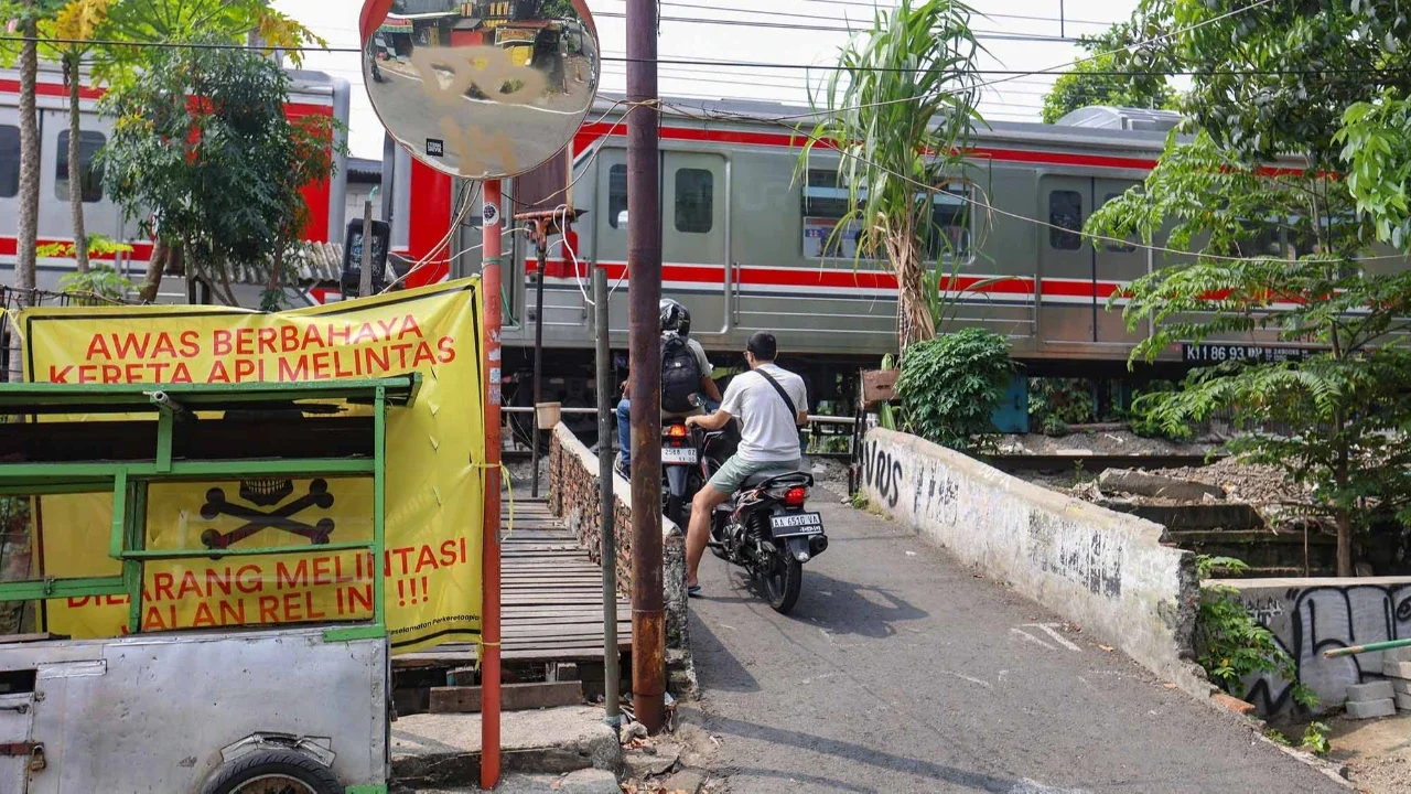 Pengendara melintas di samping spanduk peringatan dan larangan melintas di perlintasan liar jalur kereta api di kawasan Tebet, Jakarta, Jumat(15/05/2026).