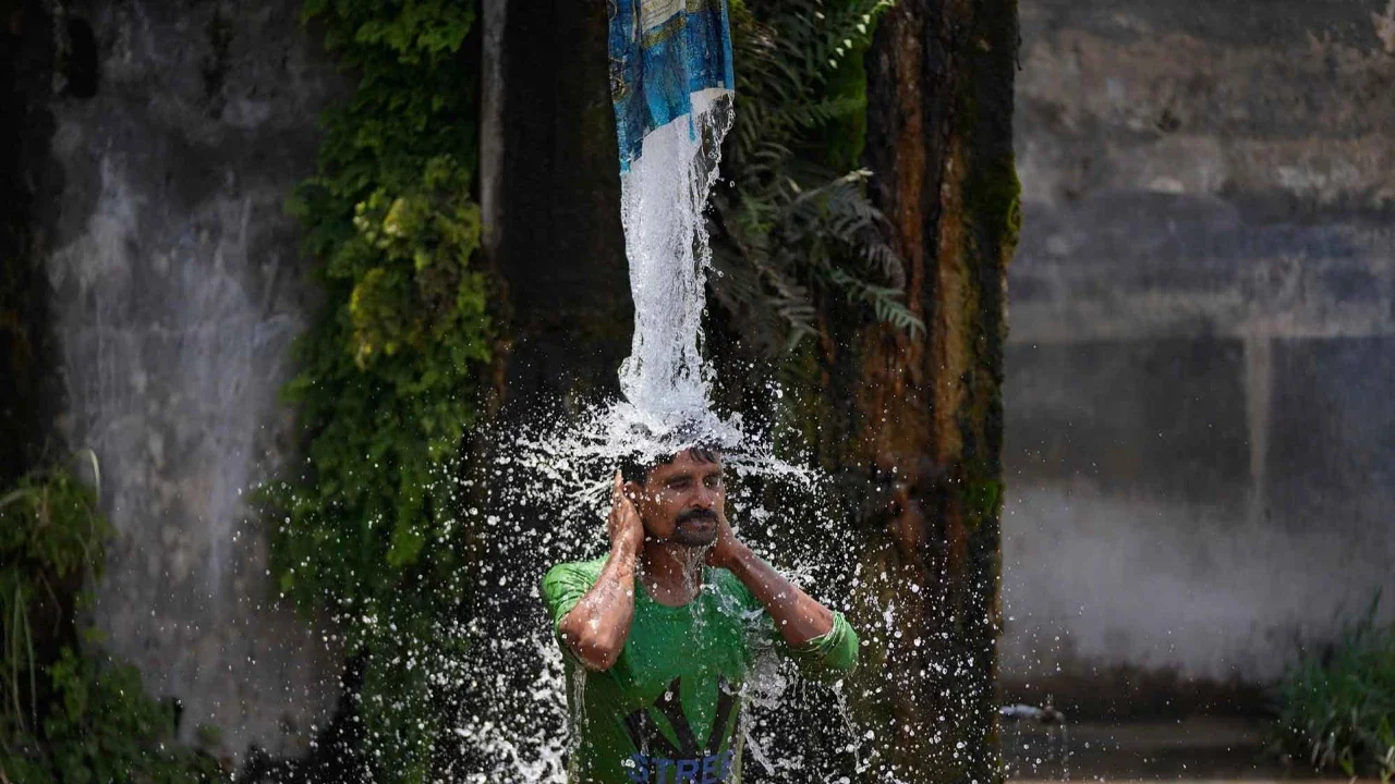 Seorang pria mandi menggunakan keran air pinggir jalan untuk mendinginkan diri di hari yang panas di pinggiran Jammu, India, Selasa, (19/05/2026).