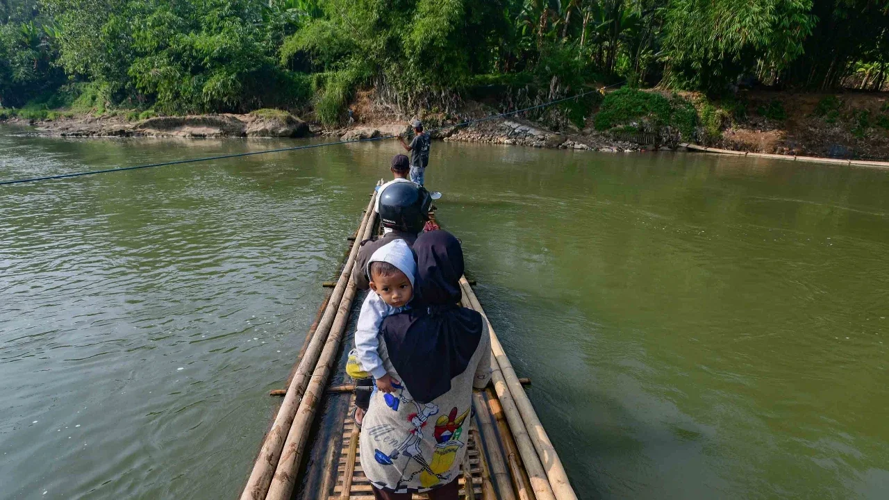 Warga dengan kendaraan motornya menggunakan rakit bambu untuk menyeberangi Sungai Cisadane di kawasan Ciseeng, Bogor, Jawa Barat, Kamis (11/06/2026).