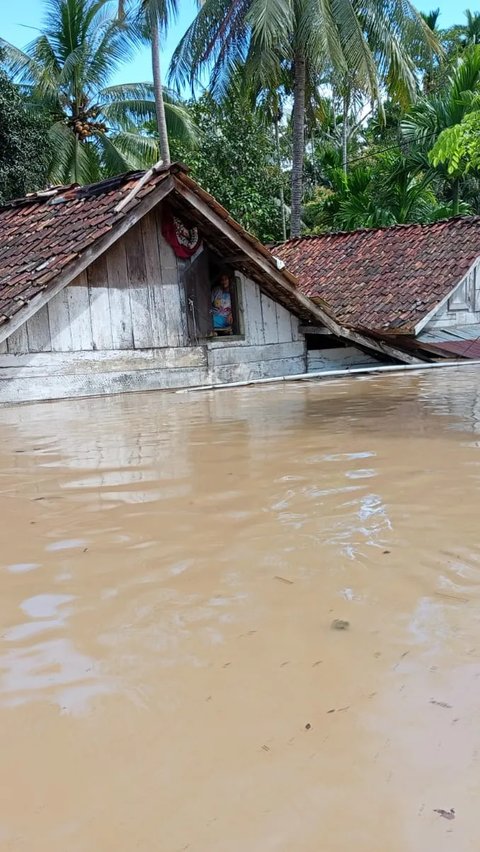 Seorang korban banjir mengintip dari jendela rumah. Nampak separuh badan rumah warga terendam air