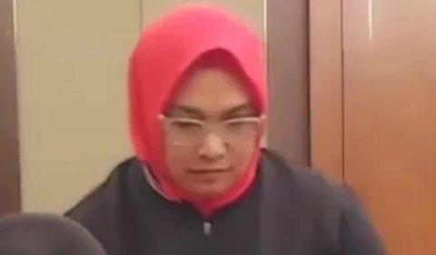 Dalam video, Tri terlihat mengenakan kerudung merah dan berjaket hitam.