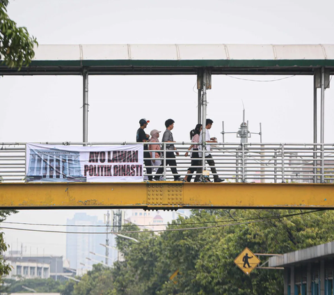 Sejumlah warga berjalan pada jempatan penyeberangan orang yang terdapat sebuah spanduk bertuliskan 