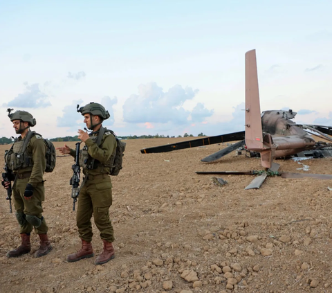 Militer Israel berdiri di sekitar bangkai helikopter CH-53 Yasur Israel pada (15/10/2023) yang dilaporkan ditembak oleh pasukan Hamas dengan rudal anti-tank.<br>