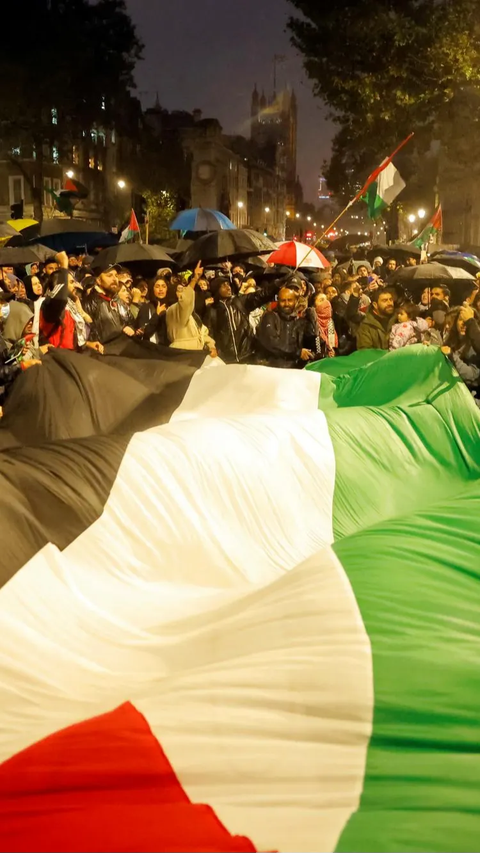 Bendera Palestina berukuran besar mereka bentangan di Downing Street selama aksi solidaritas tersebut.