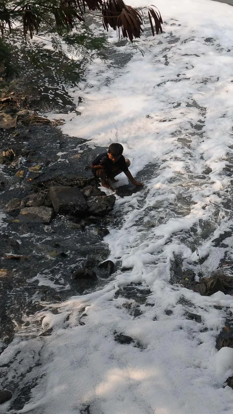 Seorang anak mencuci baju di aliran Kanal Banjir  Barat Ciliwung (KBBC) yang tercemar libah busa rumah tangga di Jakarta, Senin (23/10/2023). <br>