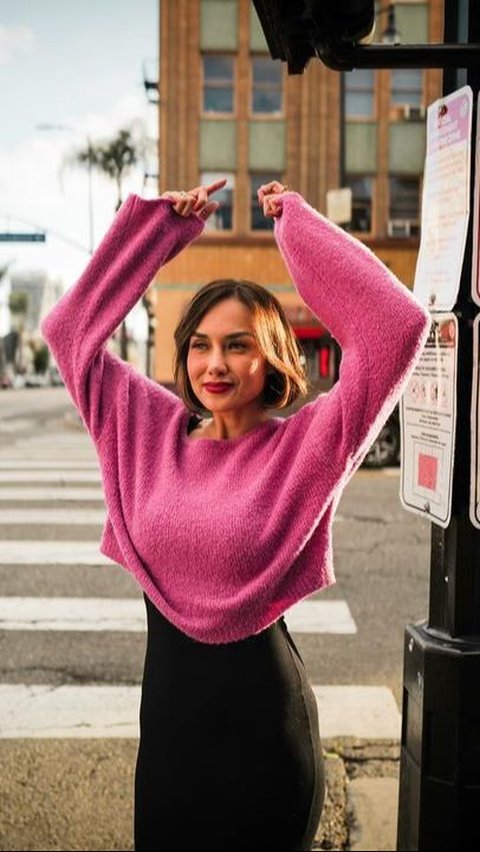 Sara memadukan terusan hitam dengan sweater warna pink.