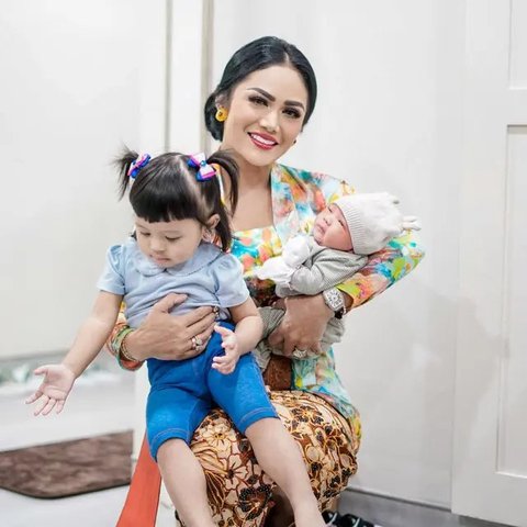 Krisdayanti elegan dalam kebaya dan batik, menggendong kedua cucunya.