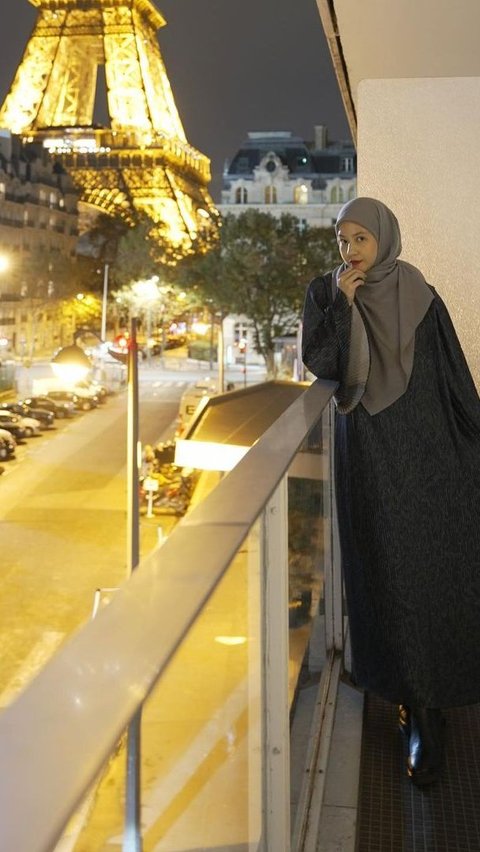 Natasha shared a picture with the background of the Eiffel Tower. She is seen wearing a black dress with a dark green pattern, combined with a gray-colored hijab.