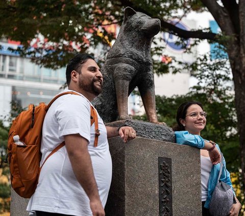 Orang-orang berpose untuk berfoto di samping patung Hachiko di depan Stasiun Shibuya, Tokyo, Senin (6/11/2023). Hachiko, anjing yang populer di kalangan pelancong Jepang, akan berusia 100 tahun pada November 2023 ini. Yuk, simak kembali kisahnya yang bikin haru!