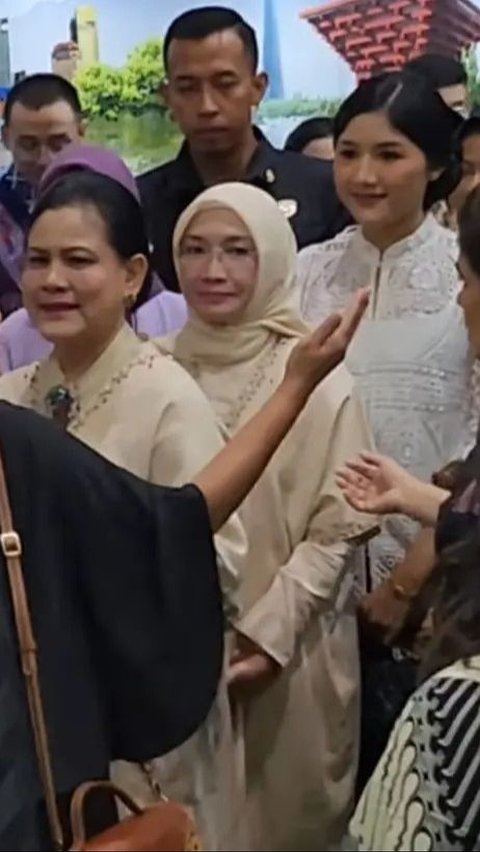 Erina memukau dengan blus brokat putih yang memiliki kerah elegan saat menemani Iriana yang mengenakan pakaian coklat.