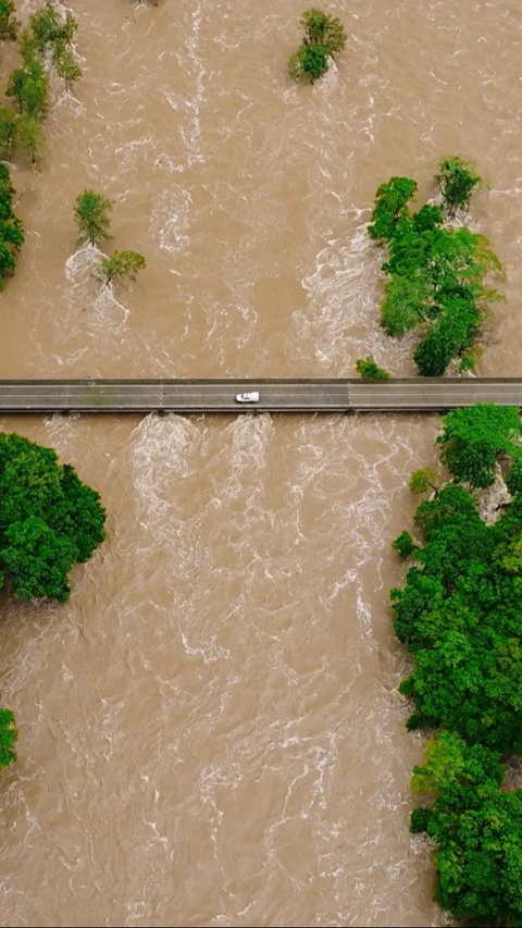 Tampak sebuah mobil melintas di jembatan di atas Sungai Barron yang meluap di Cairns, Queensland.