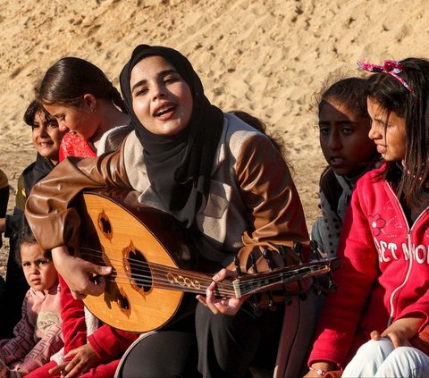 Musisi cantik Pelestina, Ruaa Hassouna memainkan musik untuk anak-anak di Rafah, Jalur Gaza bagian selatan, pada 18 Desember 2023. Aksi ini dilakukan untuk menghibur dan mendukung kesehatan mental anak-anak Jalur Gaza dari trauma kengerian perang.