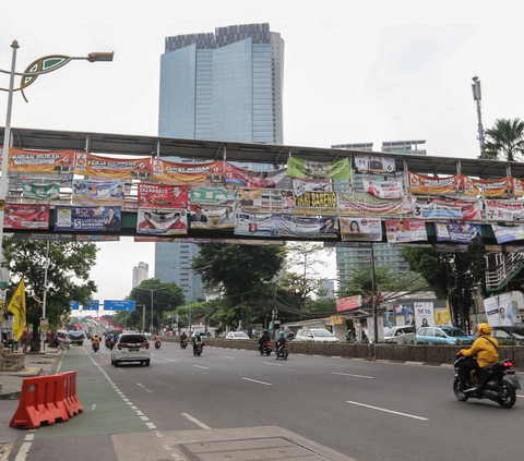 Kendaraan melintas di bawah Jembatan Penyeberangan Orang (JPO) yang tertutup oleh deretan alat peraga kampanye (APK) Pemilu 2024 di Jakarta, Rabu (27/12/2023).<br>