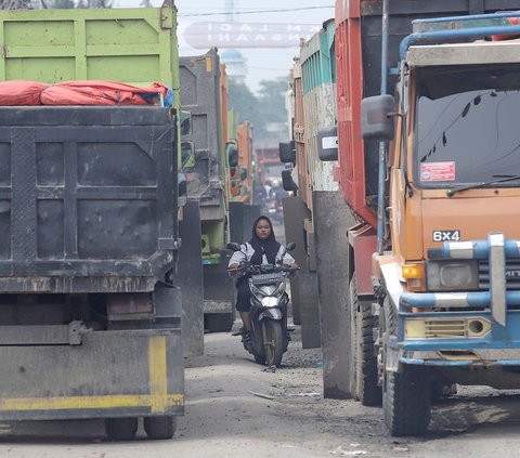 Seorang wanita mengendarai sepeda motor di antara truk tambang yang terjebak macet di Jalan Raya Parung Panjang, Bogor, Jawa Barat, Sabtu (9/12/2023). Kemacetan parah di kawasan Parung Panjang ini terjadi karena aksi demo supor truk yang digelar pada Jumat (8/12) malam.