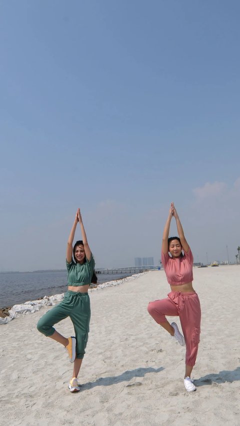Dua wanita cantik yoga di pantai pasir putih.
