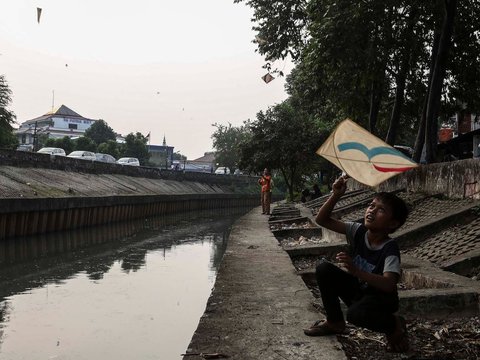 FOTO: Ruang Terbuka Hijau Minim, Anak-Anak di Jakarta Main Layang-Layang di Pinggir Kali