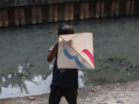 FOTO: Ruang Terbuka Hijau Minim, Anak-Anak di Jakarta Main Layang-Layang di Pinggir Kali