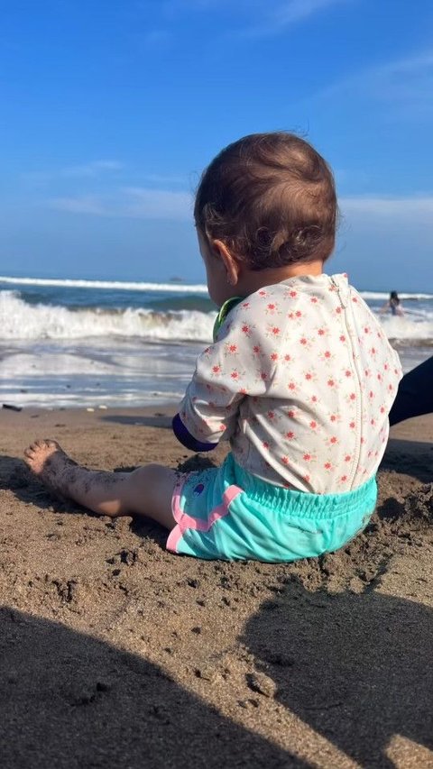 Potret Baby Djiwa sedang duduk di atas pasir pantai.