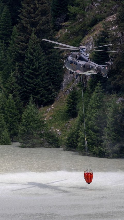 Helikopter Super Puma Angkatan Udara Swiss saat mengambil air dari Stausee Gibidum untuk memadamkan api yang membakar lahan hutan di wilayah pegunungan Bitsch dekat Brig, Swiss, Selasa (18/7/2023).