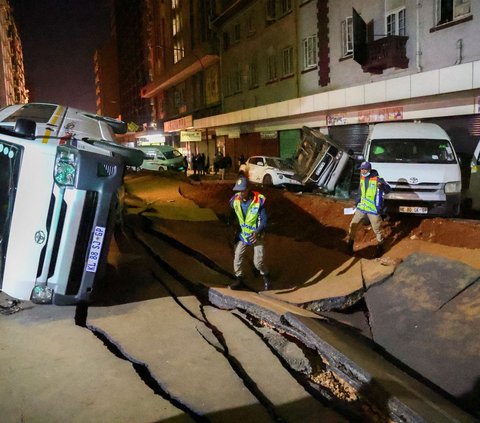 Sejumlah petugas polisi memeriksa keadaan mobil yang terbalik dan jalan yang rusak setelah ledakan gas bawah tanah terjadi di distrik pusat bisnis Johannesburg, Afrika Selatan (19/7/2023).
