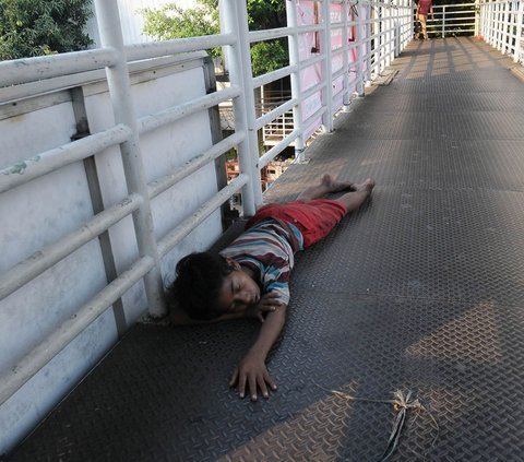 Seorang anak jalanan tampak tertidur di atas sebuah jembatan penyeberangan orang (JPO) di kawasan Glodok, Jakarta, pada Sabtu (22/7/2023) siang. Begini potretnya!