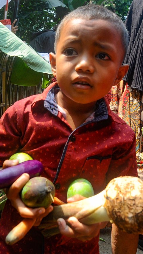 Ekspresi seorang anak yang berhasil mendapatkan beberapa buah setelah ikut rebutan hasil panen.