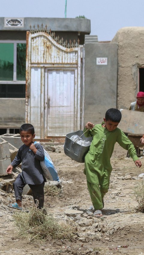 Anak-anak Afghanistan membawa barang-barang mereka setelah banjir bandang menyapu daerah Khair Abad di provinsi Ghazni.  Mereka mengungsi sementara karena rumah yang mereka tempati rusak akibat banjir bandang.