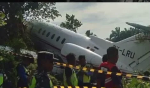 Nampak pesawat jatuh dengan sejumlah petugas berada di lokasi. Juga terdapat garis hitam putih terpasang. Pada badan pesawat juga terdapat tulisan LRU.