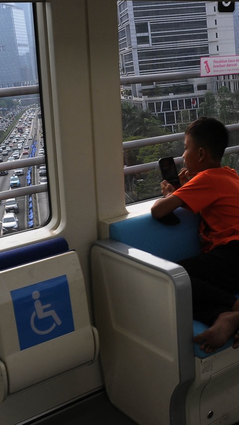 Seorang penumpang anak tampak menikmati perjalanan dengan LRT Jabodebek sambil memotret pemandangan ibu kota dengan kamera ponselnya.