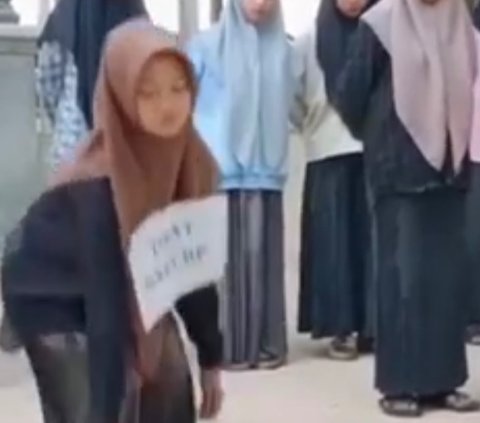 Santriwati ini terllihat berdiri di depan teman-temannya yang lain. Ia dihukum lantaran membawa HP di pondok pesantren. Pondok pesantren ini menetapkan aturan tak boleh membawa telepon genggam.