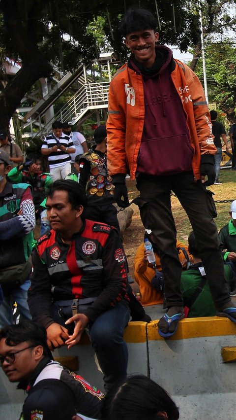 Massa Ojol berdiri di atas barikade beton saat berunjuk rasa di Jalan Medan Merdeka Barat di kawasan Patung Kuda.