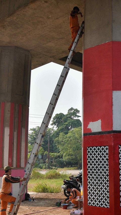 Petugas Penanganan Prasarana dan Sarana Umum menggunakan tangga saat melakukan pembuatan mural pada tiang penyangga Tol Becakayu di kawasan Cipinang Besar Selatan.