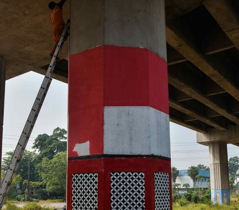 Petugas PPSU saat melakukan pemolesan tiang penyangga Tol Becakayu dengan cat warna putih merah pada tiang penyangga tol di kawasan Cipinang Besar Selatan.