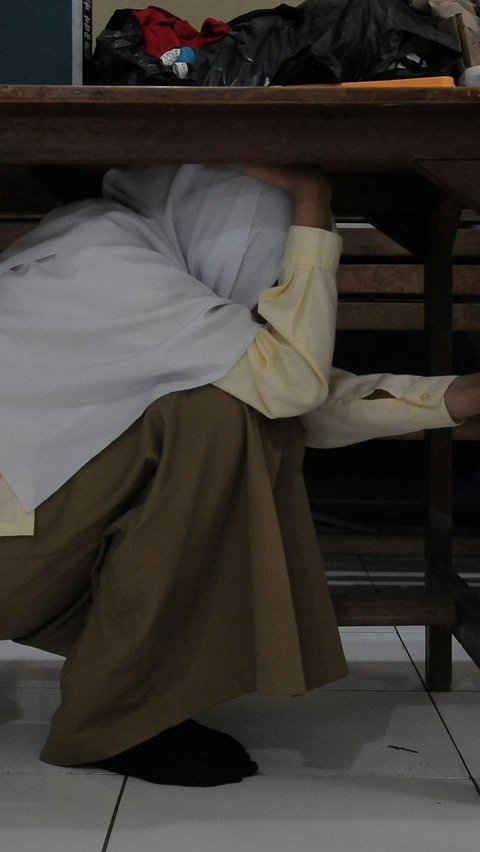 Seorang santriwati berlindung di bawah meja saat pelatihan tanggap bencana dan kebakaran di Madrasah Aliyah Swasta Persatuan Islam (MAS Persis) 69, Matraman.