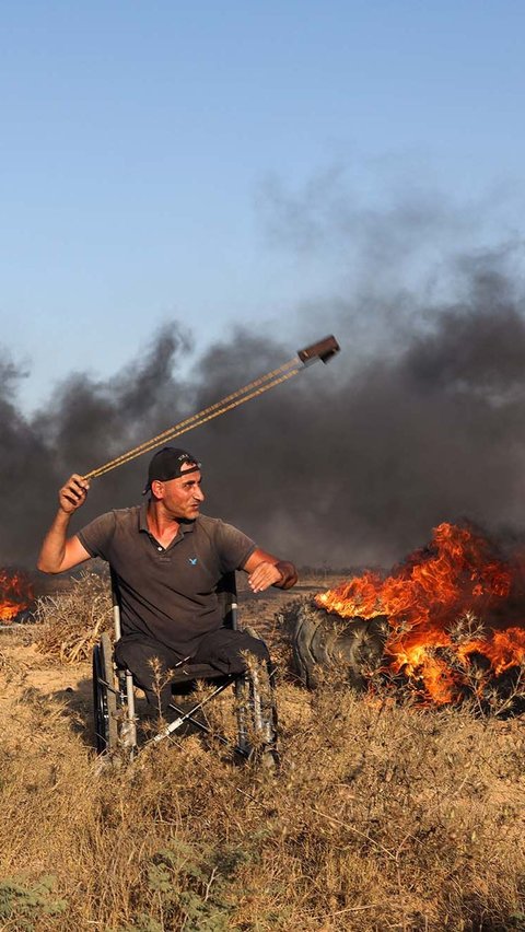 Aksi pria Palestina berkursi roda saat melemparkan batu ke arah tentara Israel.