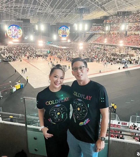 Yuanita Christiani bersama suami mengenakan t shirt hitam Coldplay dipadukan celana hitam.