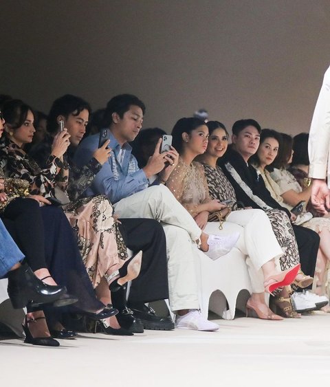 Ibu dan anak duduk berdampingan dengan serius melihat koleksi Spring Summer 2025 dari Biyan yang sedang dipertontonkan di atas catwalk.<br>