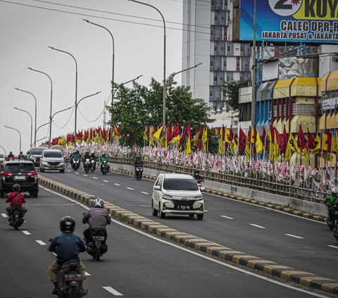 Sejumlah pengendara melintas di flyover yang dipenuhi bendera partai politik di Jakarta, Senin (15/1/2024).