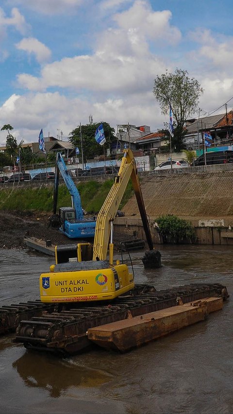 Pekerja menggunakan ekskavator untuk mengeruk material lumpur yang mengendap di Kali Ciliwung, Jakarta, Selasa (16/1/2023).