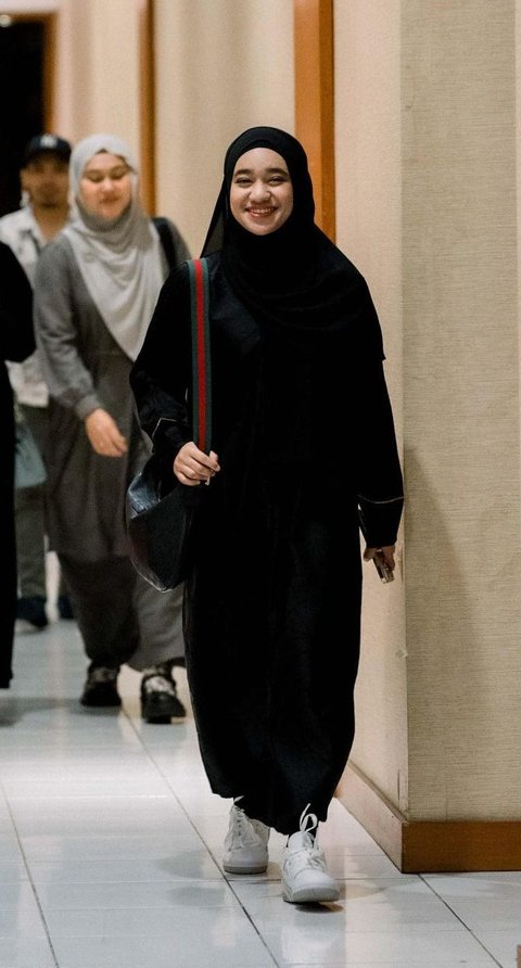 Nabila is wearing a black gamis and hijab combined with white sneakers.