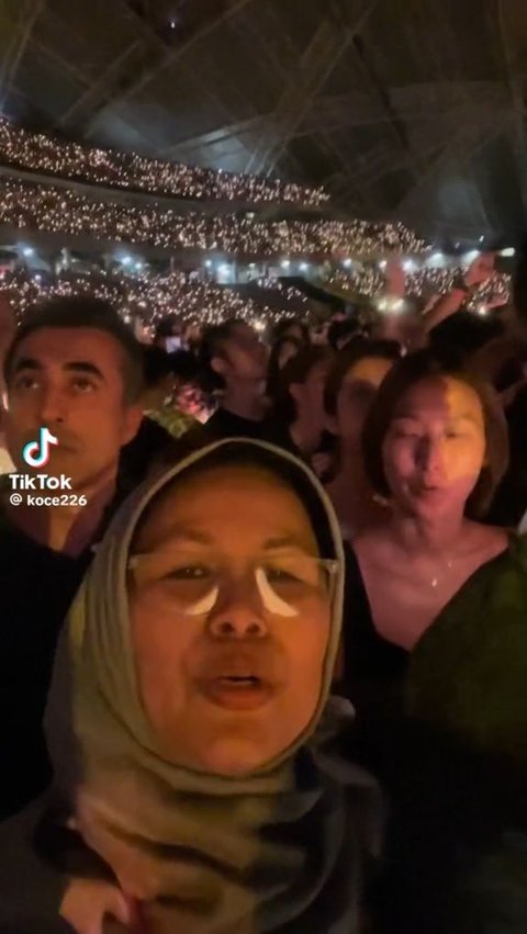 Di awal video, tampak seorang wanita paruh baya tengah berdiri di tengah puluhan ribu orang saat menonton konser Coldplay di Singapura.