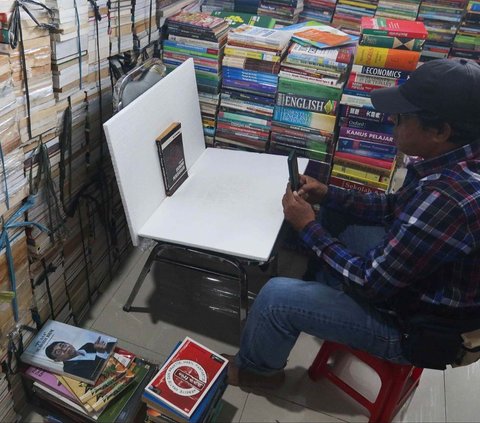 Pedagang memotret buku yang hendak dipasarkan secara online di kiosnya di Sentra Buku Pasar Kenari, Jakarta, Selasa (30/1/2024). Kondisi Pasar Kenari yang sepi pengunjung membuat pedagang buku mengalami penurunan omset. Foto: Liputan6.com/Herman Zakharia<br>