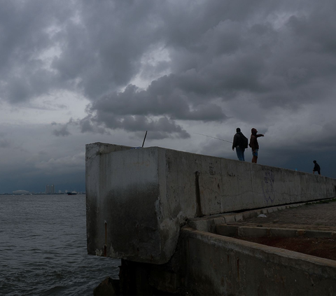Warga berdiri di atas tanggul laut Muara Baru saat awan gelar menyelimuti Jakarta pada Kamis (4/1/2024). Badan Meteorologi, Klimatologi, dan Geofisika (BMKG) melaporkan hujan bakal kembali turun di seluruh wilayah DKI Jakarta, pada Kamis, 4 Januari 2024. <br>