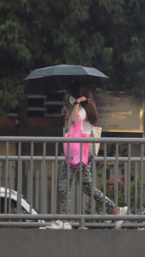Warga memakai payung saat hujan mengguyur di kawasan Sarinah, Jakarta, Sabtu (6/1/2024).
