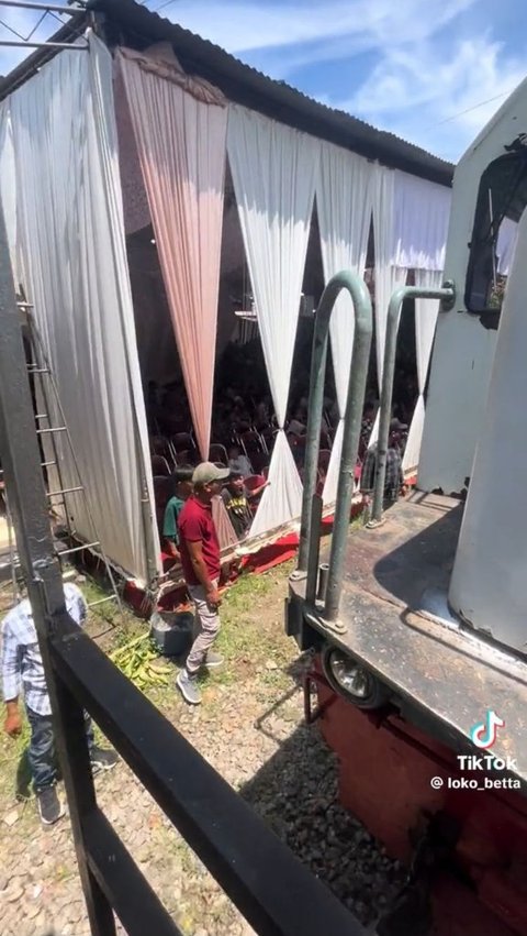 Inilah momen saat kereta langsiran melewati tenda hajatan warga. Tampak kursi-kursi berjajar di dalam tenda.