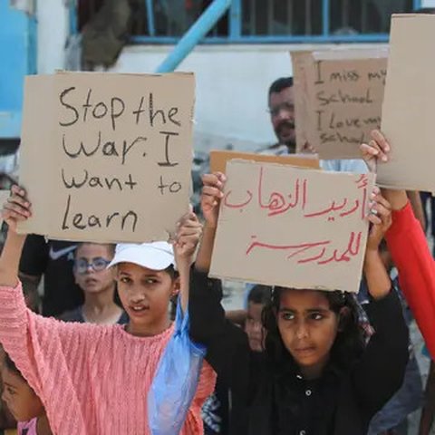 Sejumlah pelajar didampingi para aktivis Palestina mengangkat plakat saat berunjuk rasa menyerukan diakhirinya situasi perang di Gaza, di samping gedung sekolah yang rusak di Khan Yunis di Ja