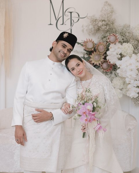 Sementara itu, mempelai pria mengenakan baju adat Melayu yang juga bernuansa serba putih, memberikan kesan elegan dan berwibawa.